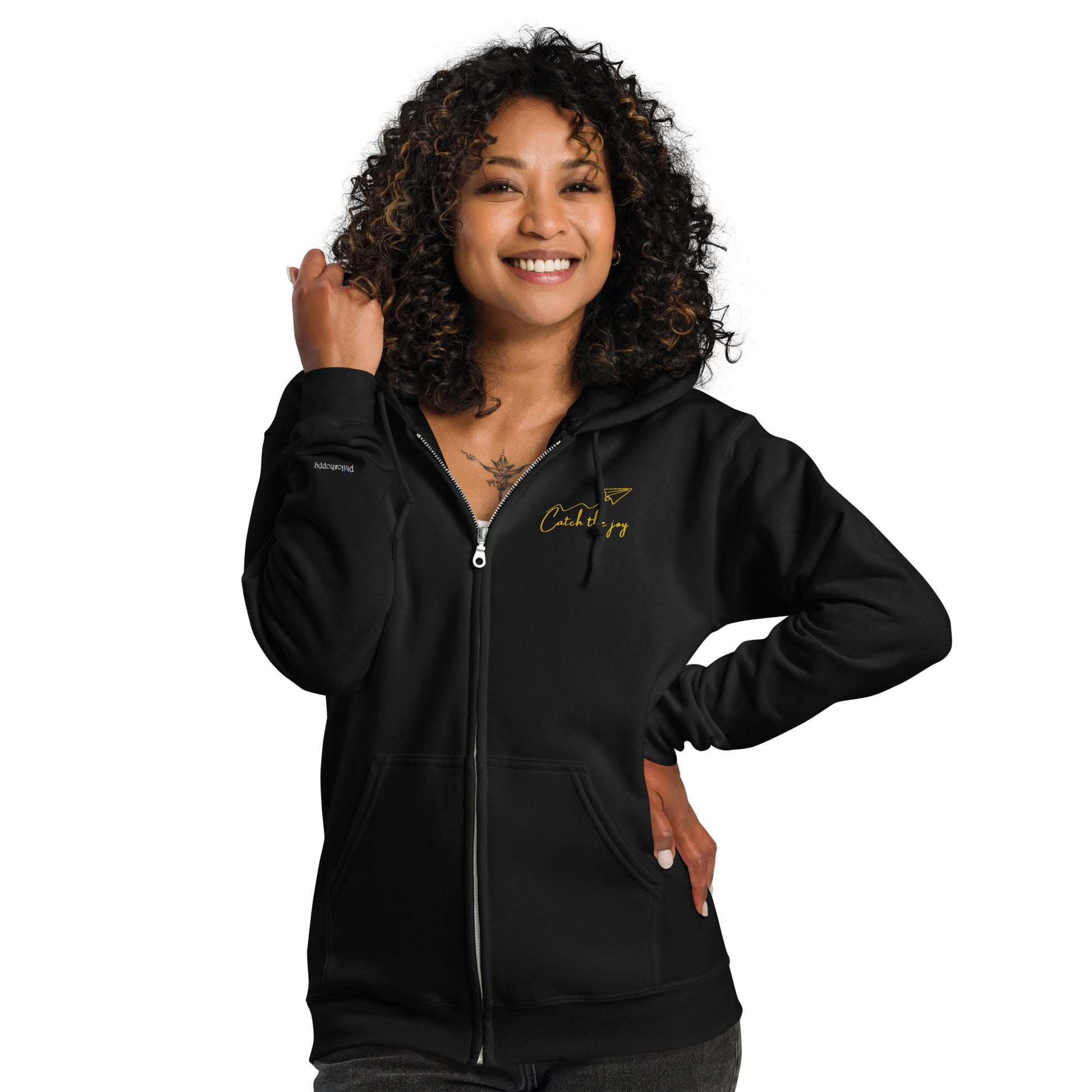 Black embroidered zipped hoodie with “Catch the Joy” text and origami plane — unisex cotton design celebrating lightness, play, and mindful living.