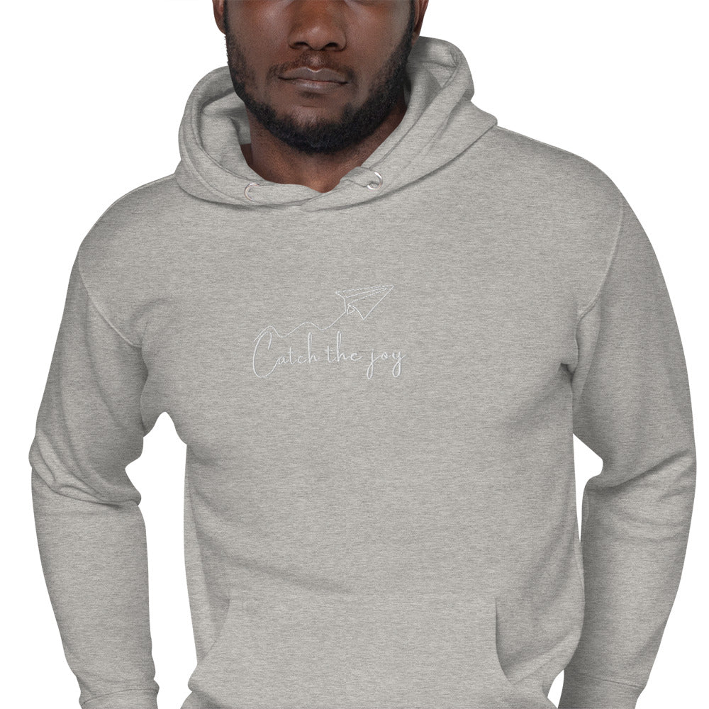 Relaxed grey hoodie featuring “Catch the Joy” embroidered text; unisex design celebrating lightness, presence, and everyday happiness.