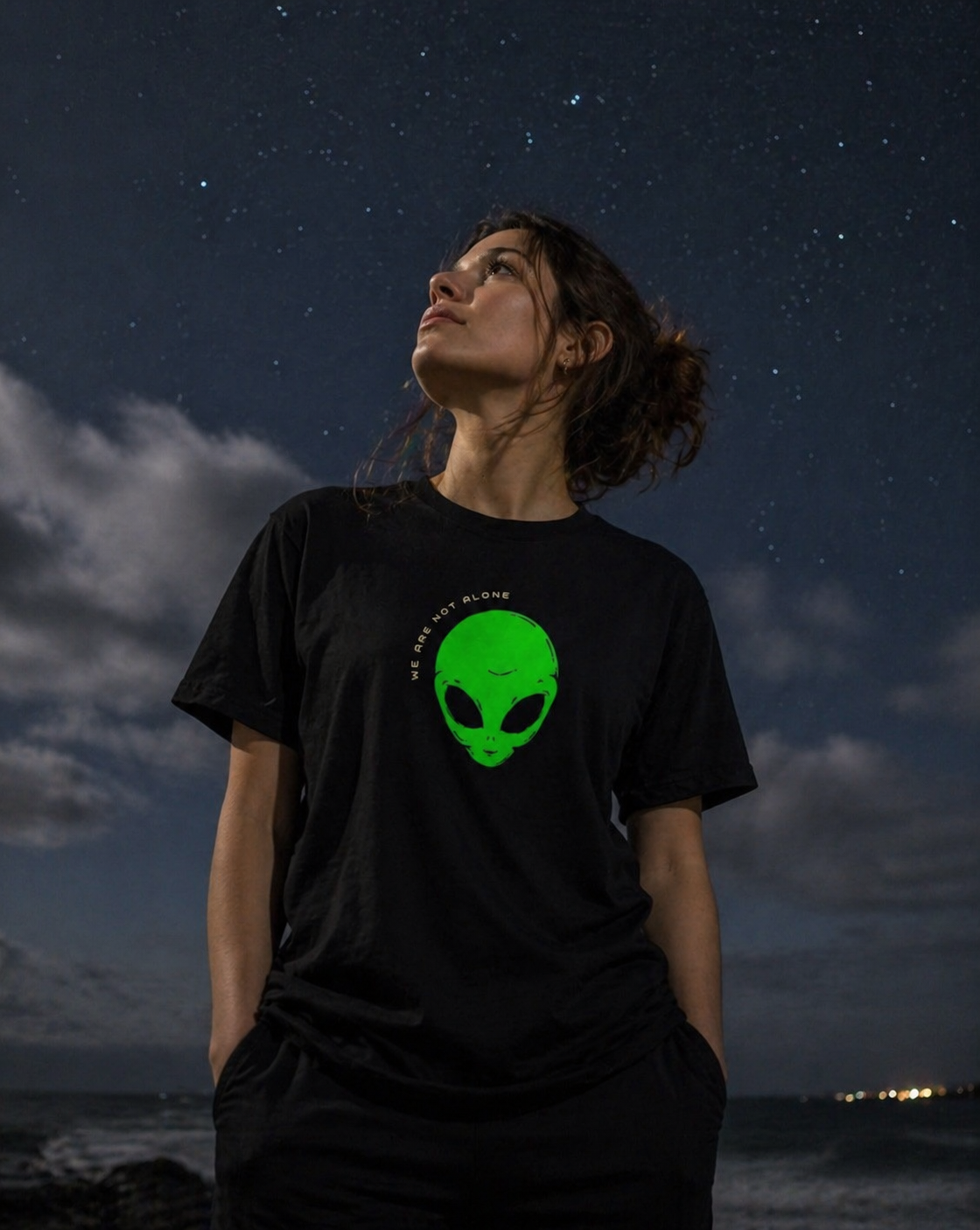 Person wearing a black t-shirt with a green alien graphic against a night sky.