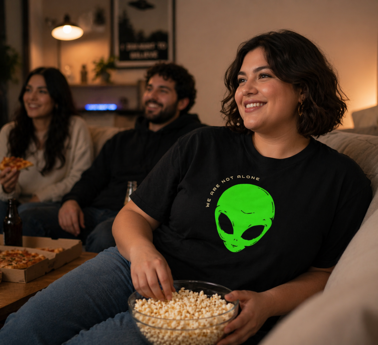 Woman in a black t-shirt with an alien graphic sitting on a couch with popcorn, surrounded by friends in a casual setting.