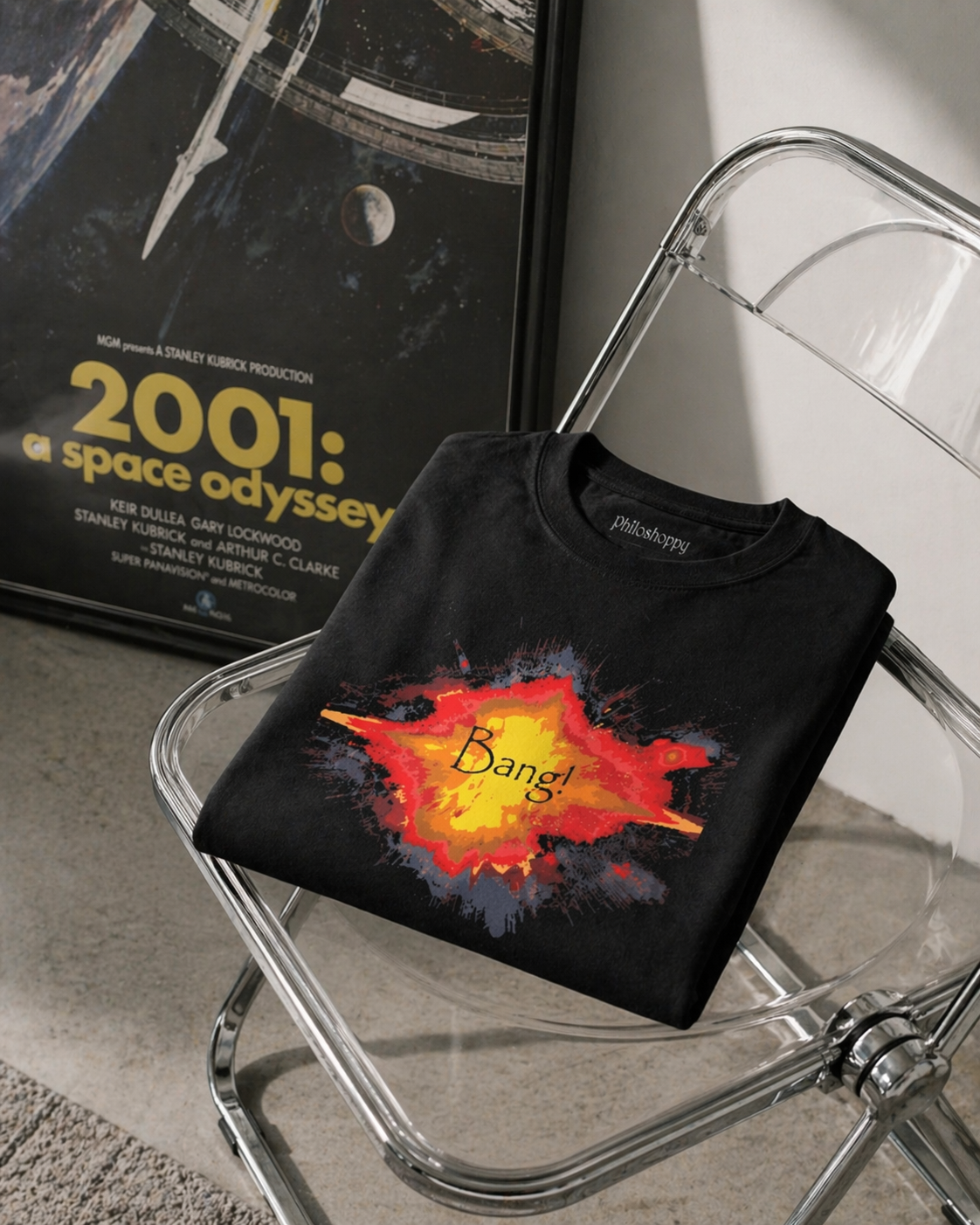 Black t-shirt with 'Bang!' design on a clear chair next to a '2001: A Space Odyssey' movie poster.