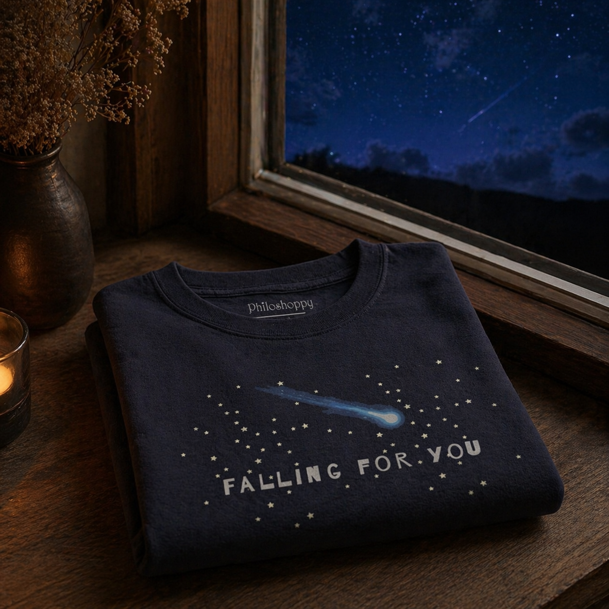 Folded navy blue t-shirt with 'Falling for You' design on a wooden surface with a window view of night sky.