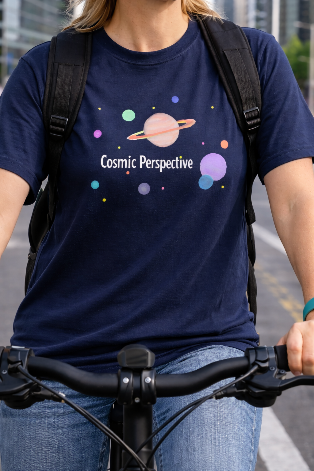 Person wearing a navy blue t-shirt with 'Cosmic Perspective' design while riding a bicycle.