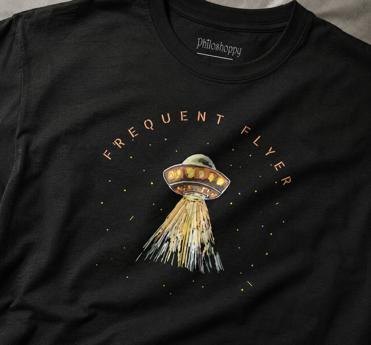 Black t-shirt close-up with a UFO graphic and 'Frequent Flyer' text on a dark background