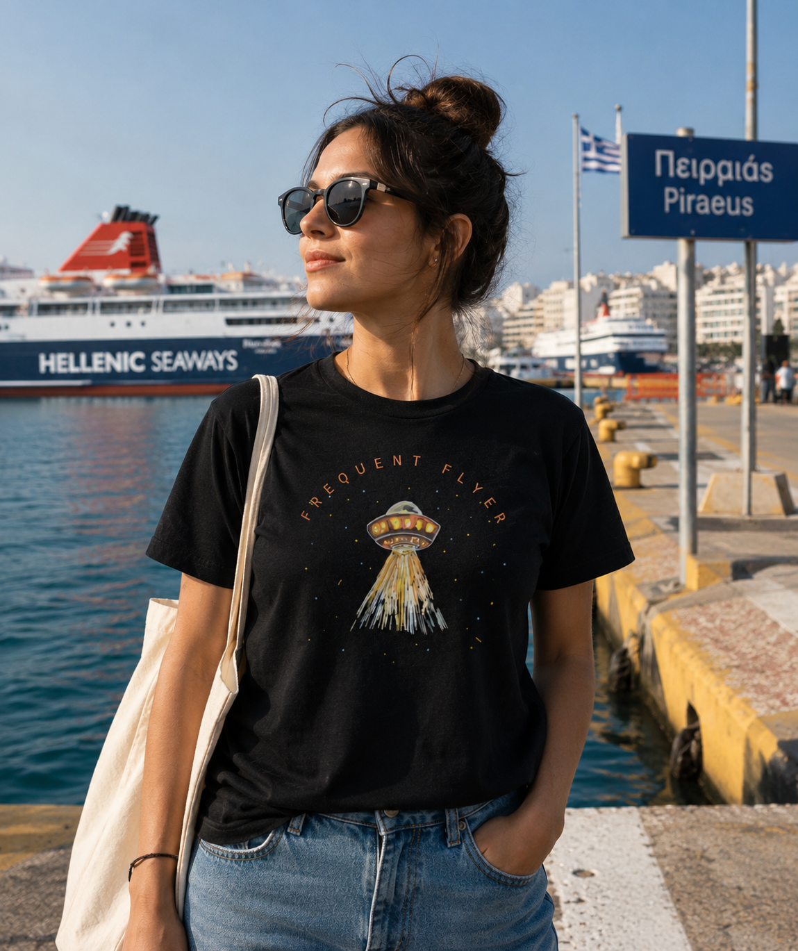 Woman wearing a black t-shirt with a graphic design by the water, with a ferry and cityscape in the background.