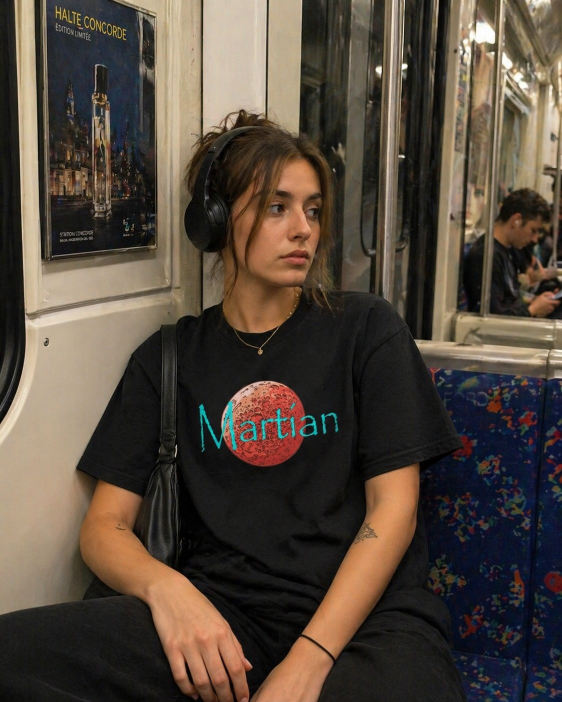 Person wearing a black t-shirt with a red  planet and blue Martian text graphic, sitting on a subway train.