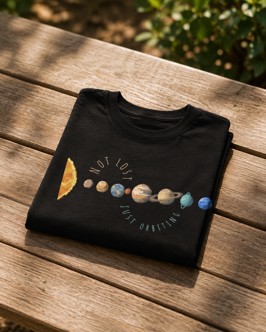 Folded black cotton t-shirt showing minimalist planet illustration with solar system design and inspirational space quote  on a wooden surface