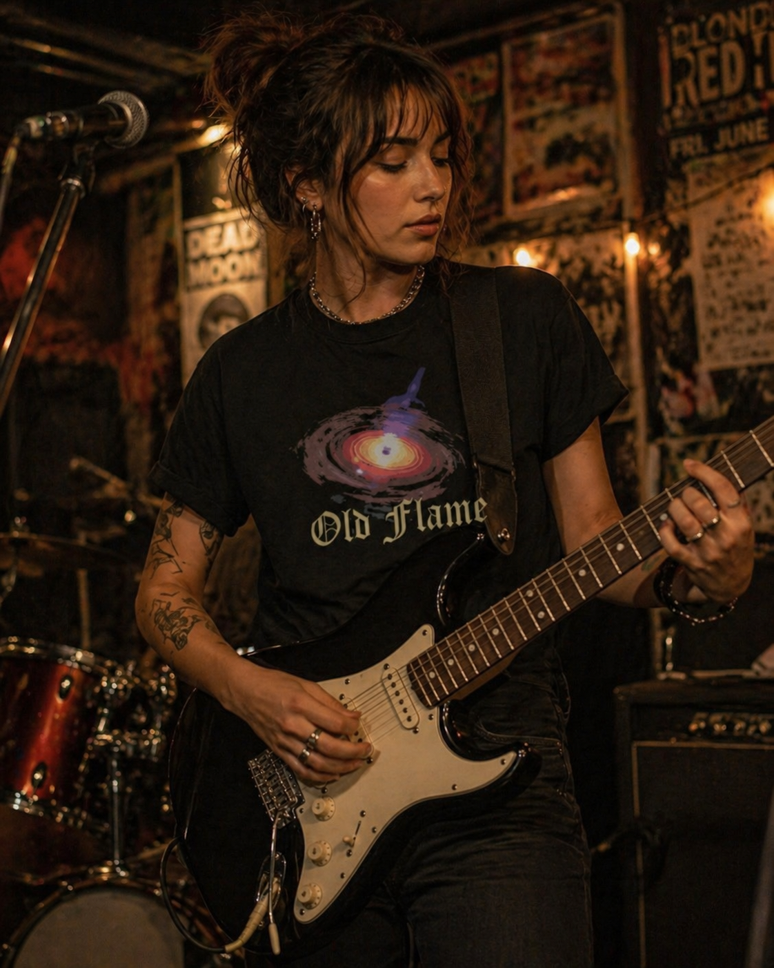 Woman wearing Philoshoppy's Black Hole unisex cotton t-shirt playing guitar in a music venue with posters on the wall.