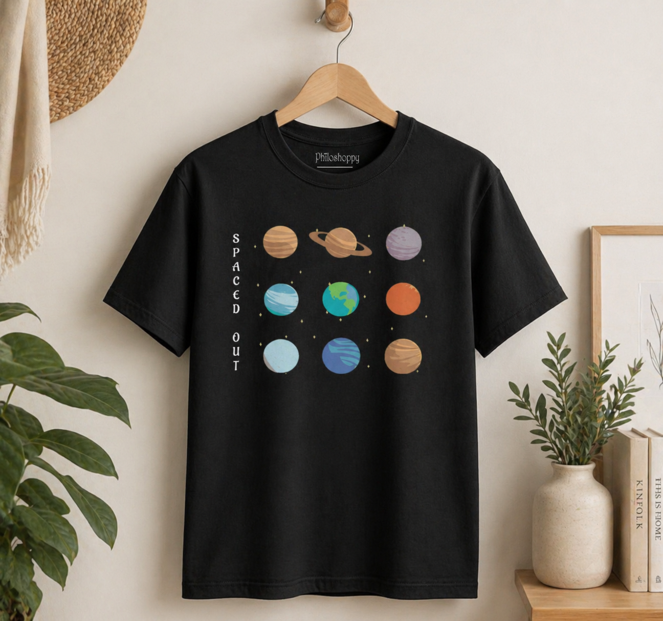 Black t-shirt with space-themed design on a hanger against a neutral wall.