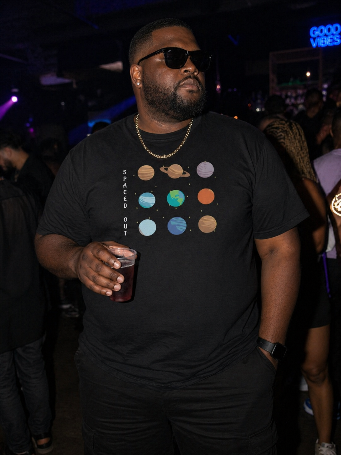 Man wearing a black t-shirt with space-themed design, holding a drink, in a dark indoor setting.