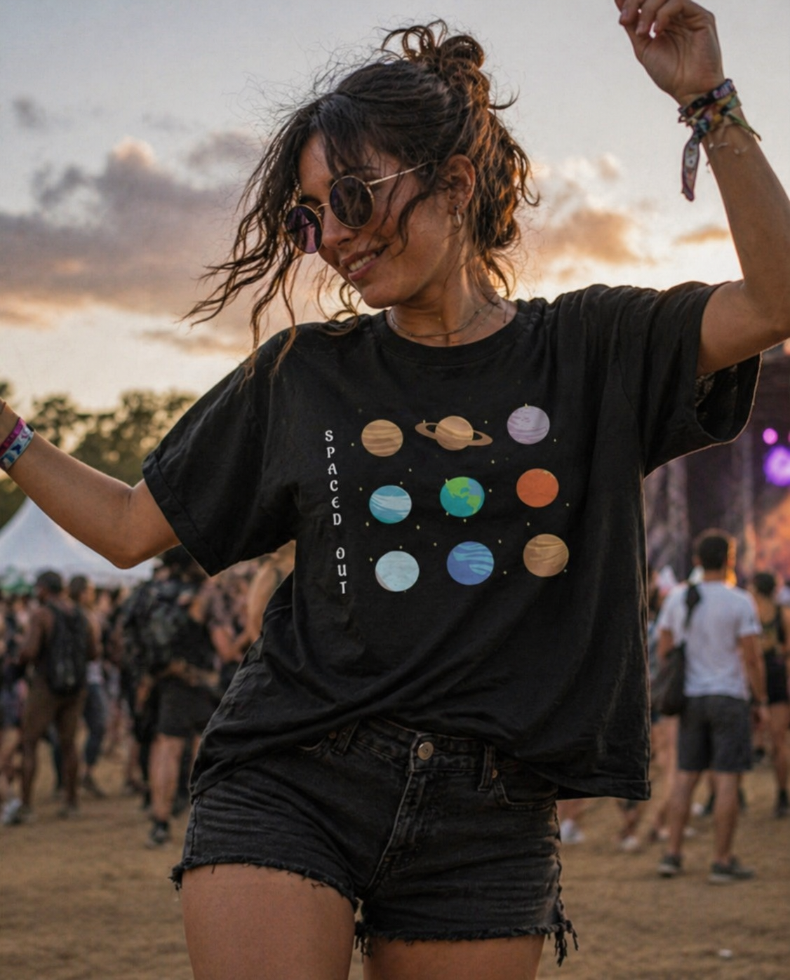 Woman wearing a black t-shirt with colorful planets and 'Spaced Out' text at a music festival.