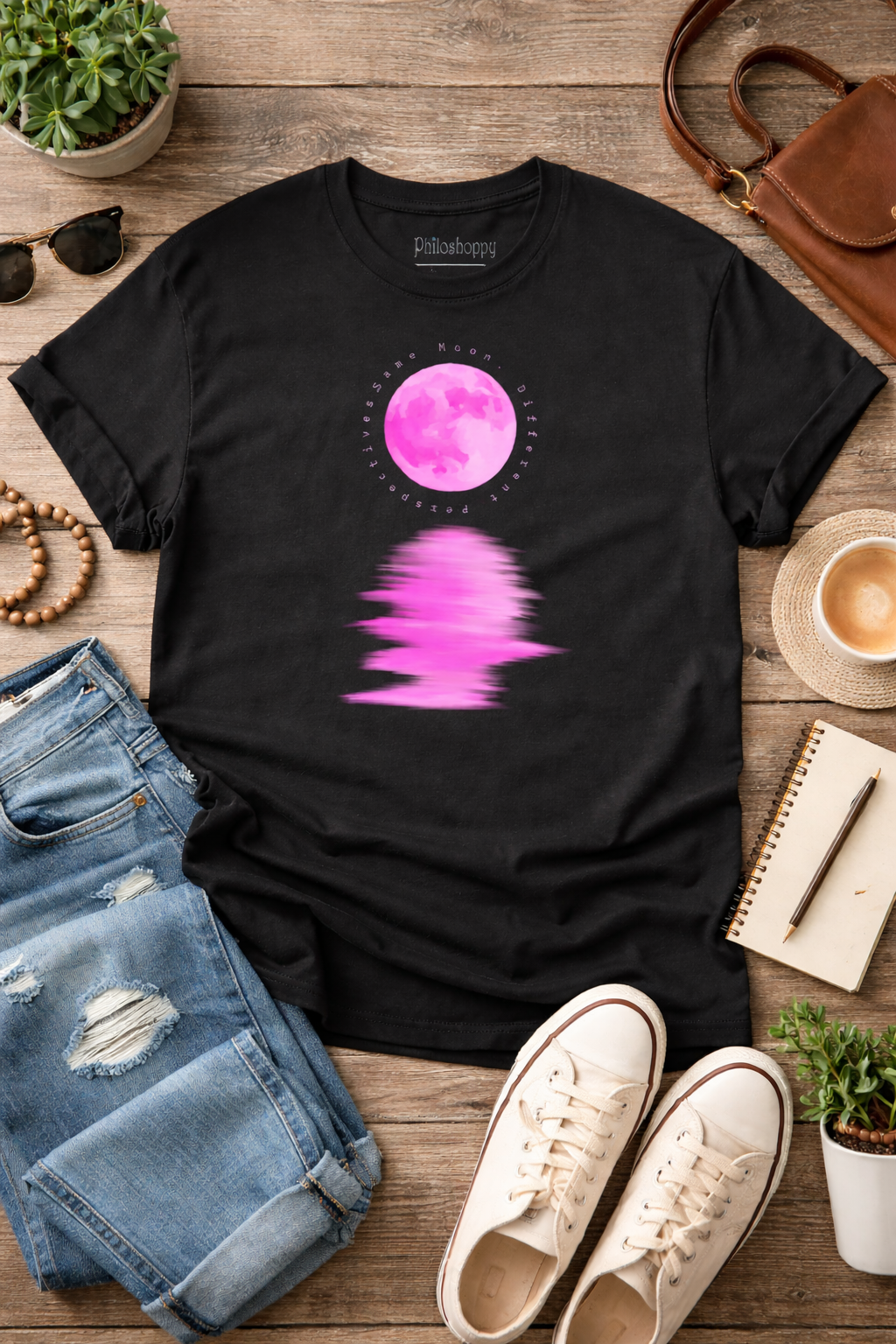 Black t-shirt with pink moon graphic on a wooden surface with jeans, shoes, and a coffee cup.
