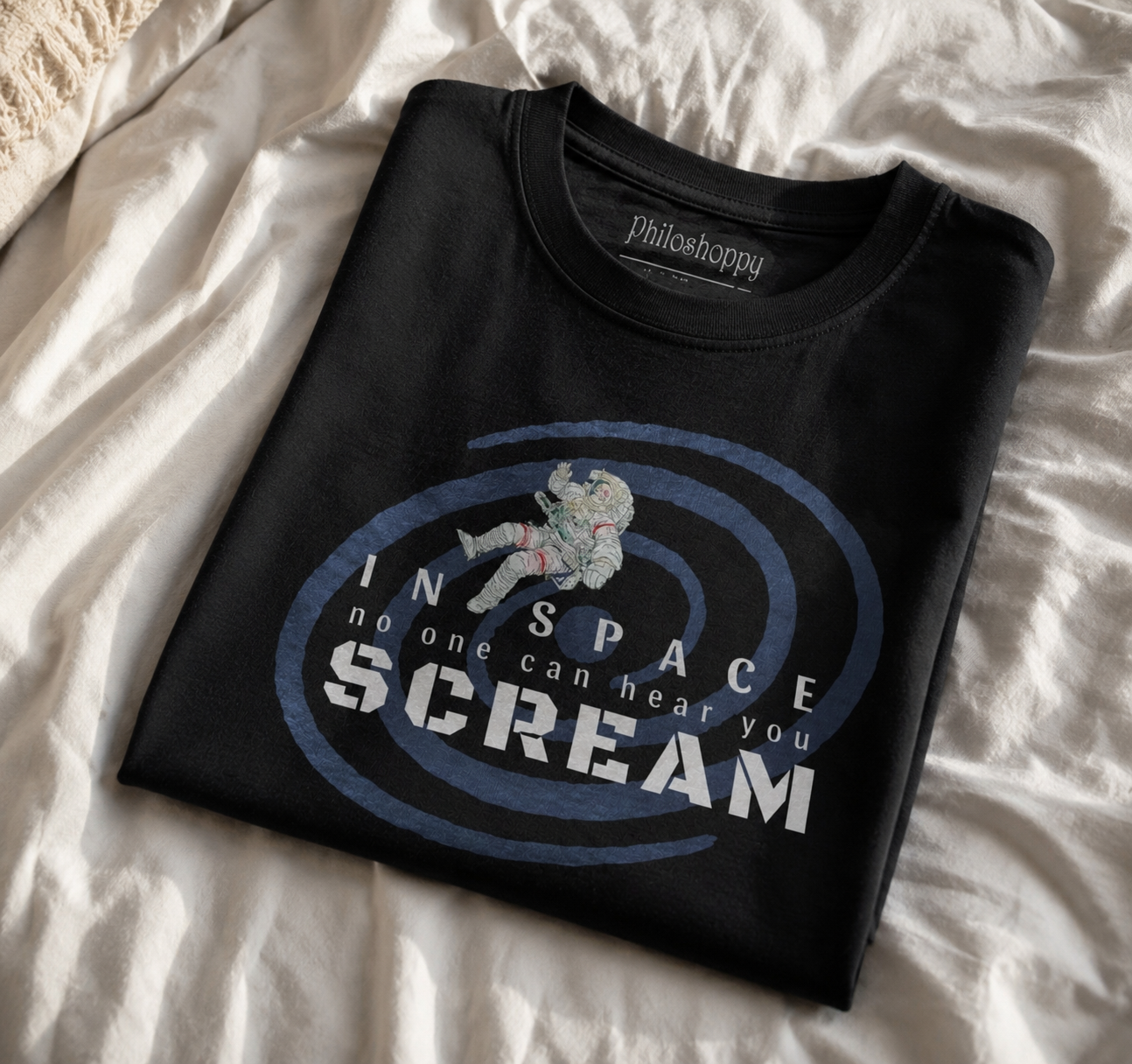 Folded black t-shirt with graphic design and text on a white bedspread